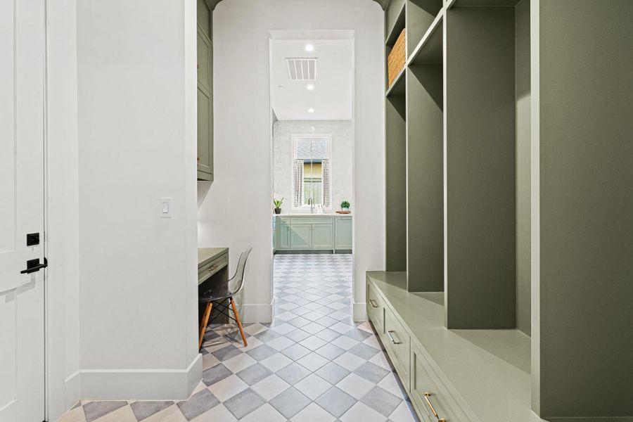 Designed for everyday functionality, the mudroom serves as an ideal drop zone between the scullery kitchen & garage. Built-in bench seating w/ individual cubbies, drawers below & additional shelving above provides organized storage, while a dedicated desk area w/ cabinetry adds versatility. Porcelain tile flooring in a checker pattern introduces a subtle design element, all paired w/ direct access to the attached garage for added convenience. Designed for everyday functionality, the mudroom serves as an ideal drop zone between the scullery kitchen & garage. Built-in bench seating w/ individual cubbies, drawers below & additional shelving above provides organized storage, while a dedicated desk area w/ cabinetry adds versatility. Porcelain tile flooring in a checker pattern introduces a subtle design element, all paired w/ direct access to the attached garage for added convenience.
