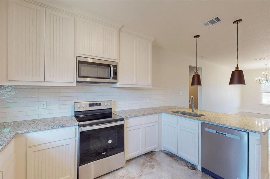 Kitchen with sink, hanging light fixtures, kitchen peninsula, stainless steel appliances, and backsplash