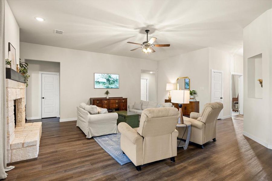 Living room featuring dark wood-style flooring, ceiling fan, recessed lighting, and a stone fireplace