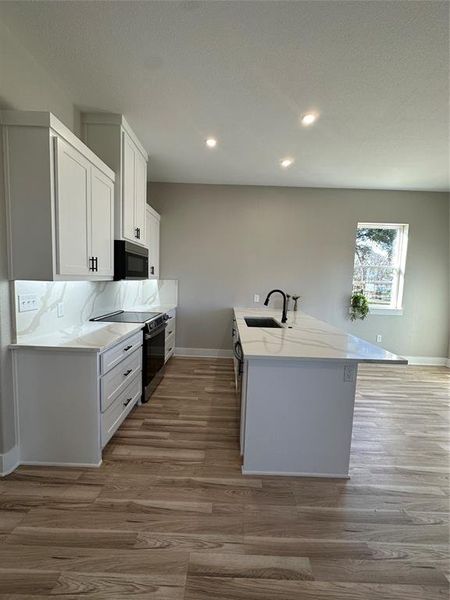 Kitchen featuring sink, light wood-type flooring, white cabinetry, tasteful backsplash, and range