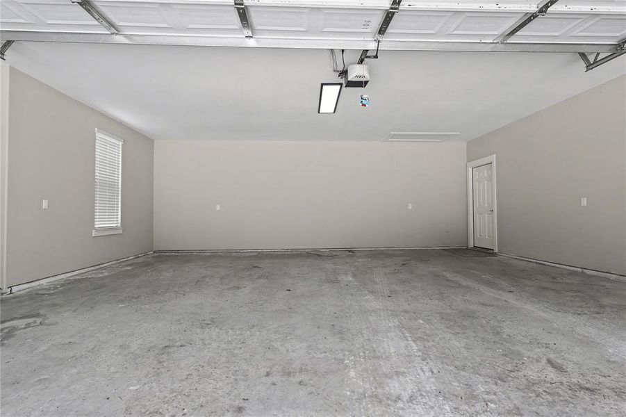 Spacious garage featuring a concrete floor, light gray walls, a window with blinds, and a white interior door