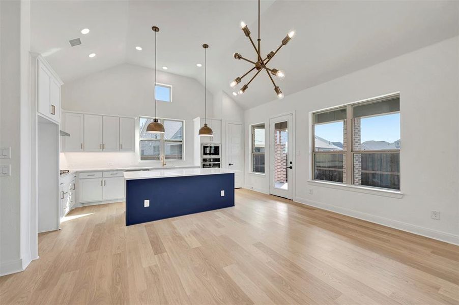Kitchen featuring white cabinets, a kitchen island, a chandelier, vaulted ceiling, and light wood-style flooring Kitchen featuring white cabinets, a kitchen island, a chandelier, vaulted ceiling, and light wood-style flooring