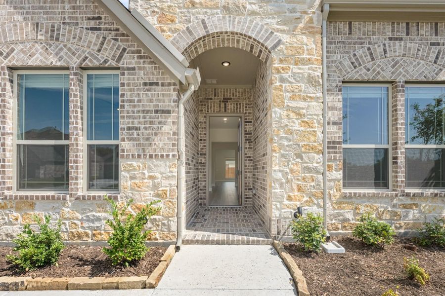 Home entrance with brick and stone exterior, arched doorway, and concrete walkway with landscaping