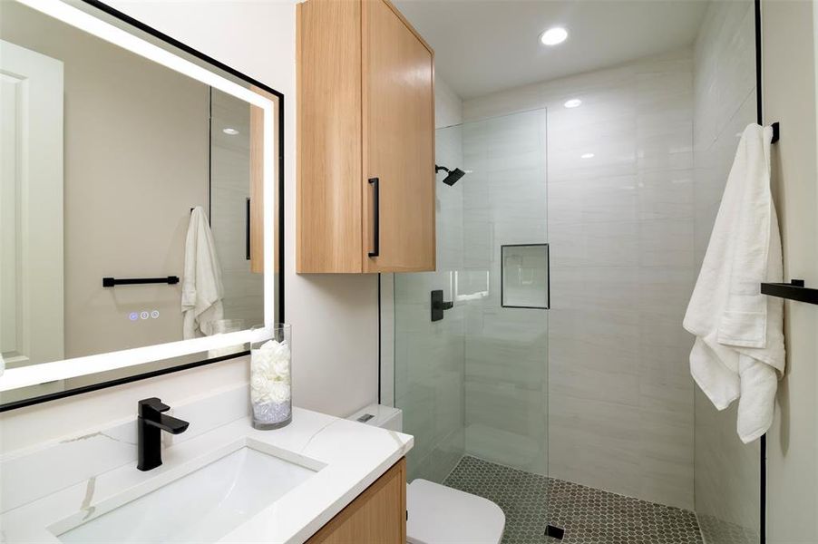 Bathroom featuring a shower with door, vanity, and toilet