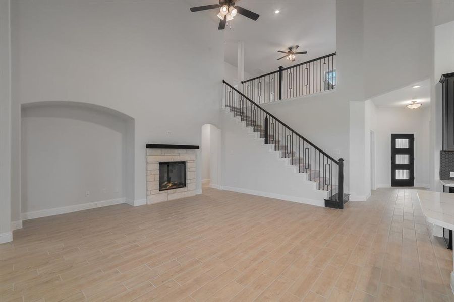 Unfurnished living room featuring ceiling fan, a towering ceiling, a stone fireplace, and light hardwood / wood-style floors