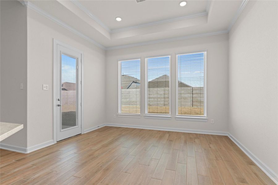 The bright breakfast area is filled with natural light from large windows, offering a lovely spot for casual meals or morning coffee, enhanced by wood like tile flooring and an open view into the main living spaces.