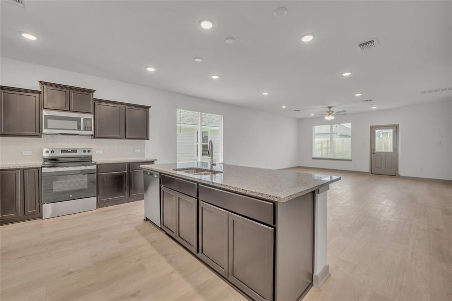 Kitchen with stainless steel appliances, recessed lighting, open floor plan, light wood-style floors, and dark brown cabinets