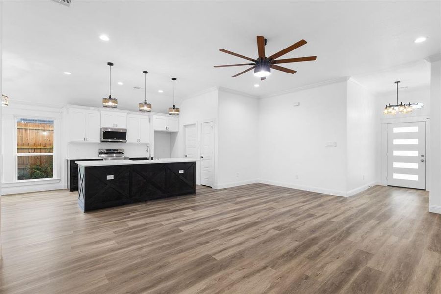 Kitchen featuring wood-type flooring, crown molding, white cabinetry, appliances with stainless steel finishes, and a kitchen island with sink