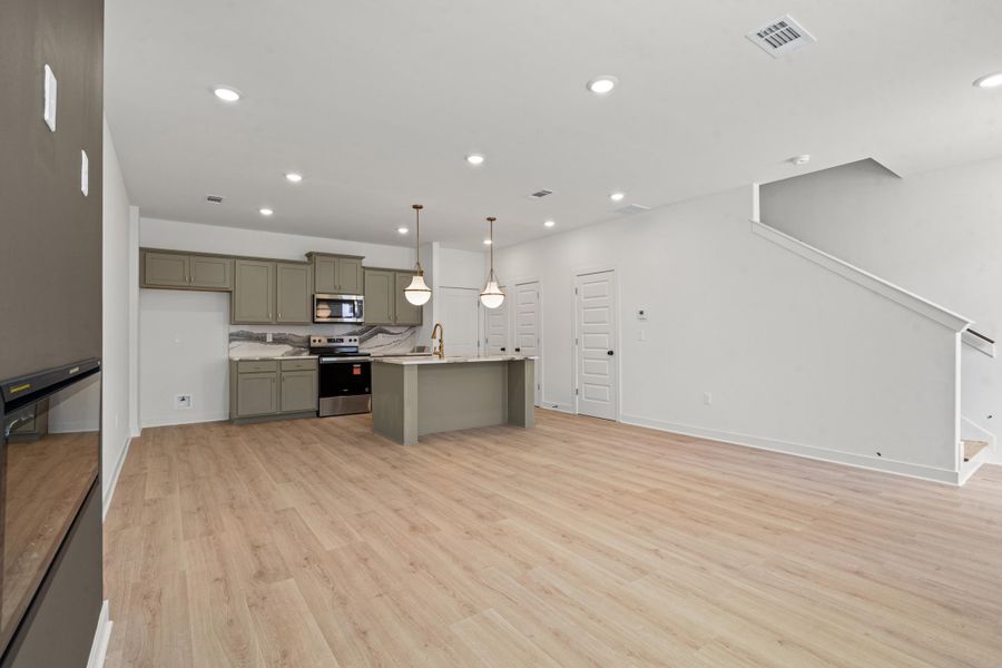 Open-concept living area featuring light wood-finish flooring, recessed lighting, and a modern kitchen with a large island