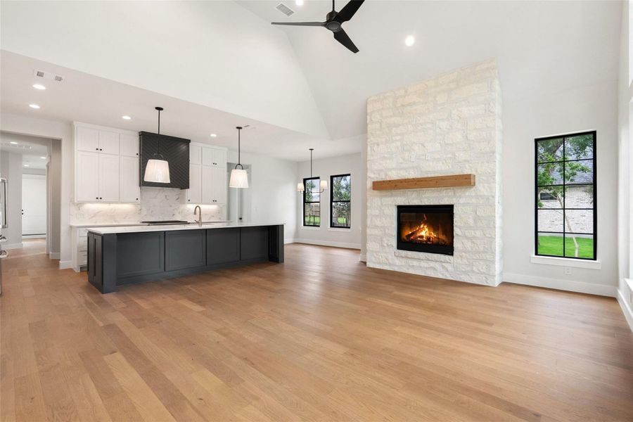 A spacious, open-concept interior unites a modern kitchen with a cozy fireplace, framed by soaring vaulted ceilings.