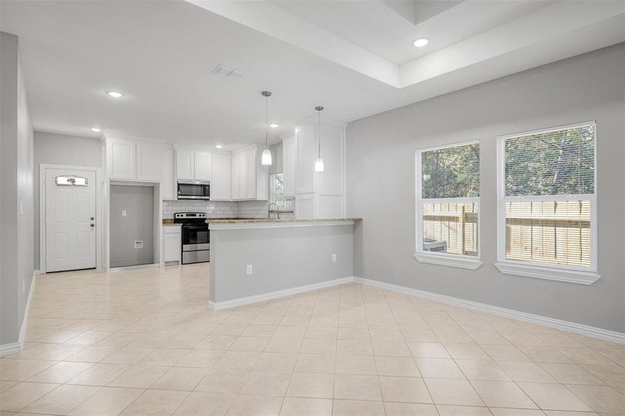 Kitchen with kitchen peninsula, light stone countertops, stainless steel appliances, pendant lighting, and white cabinetry