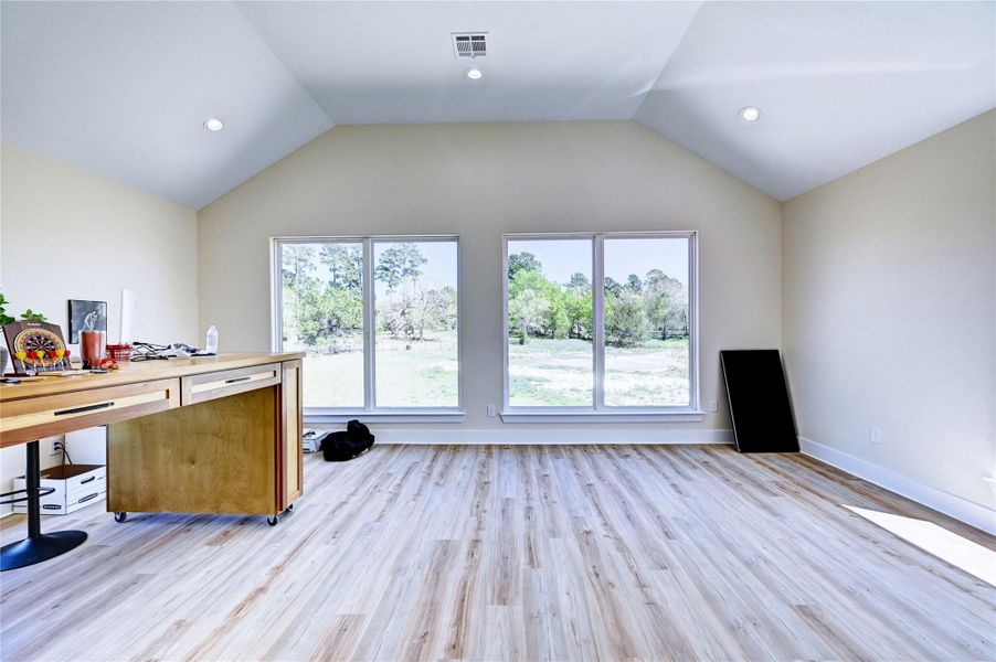 Bright and spacious room with high ceilings, wood flooring, and large windows offering scenic views of greenery. Ideal for a home office or study.