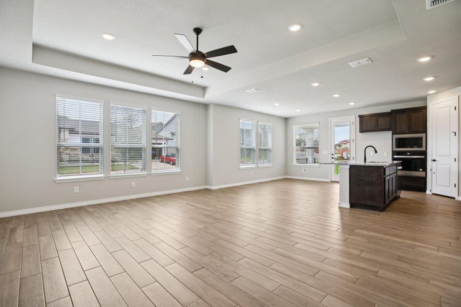 Unfurnished living room featuring a tray ceiling, a ceiling fan, light wood-type flooring, and recessed lighting