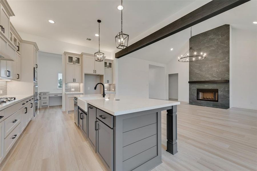 Kitchen with a high end fireplace, light wood-type flooring, sink, gray cabinets, and a kitchen island with sink