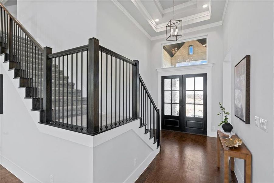 Foyer entrance with crown molding, a towering ceiling, dark hardwood / wood-style flooring, french doors, and a chandelier