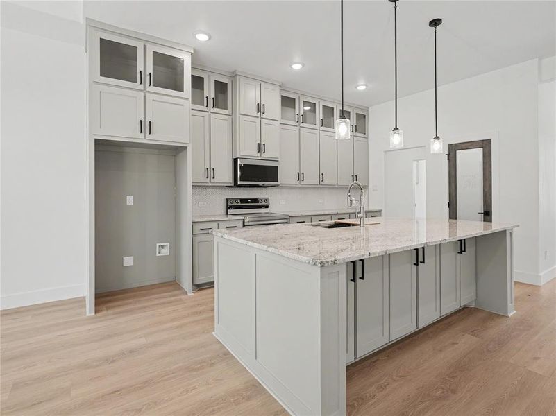 Open-concept kitchen featuring an expansive central island with a light-colored countertop, light gray cabinetry, and a subway tile backsplash Open-concept kitchen featuring an expansive central island with a light-colored countertop, light gray cabinetry, and a subway tile backsplash