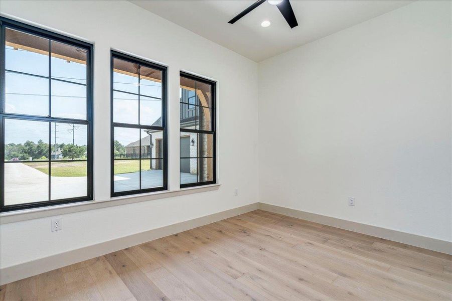 Blonde hardwood floors and a modern ceiling fan complement the bright, minimalist aesthetic of this versatile room.
