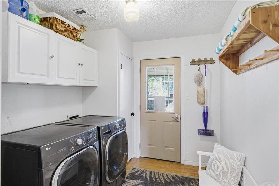 Laundry area featuring wood-finish flooring, white cabinetry with silver-tone hardware