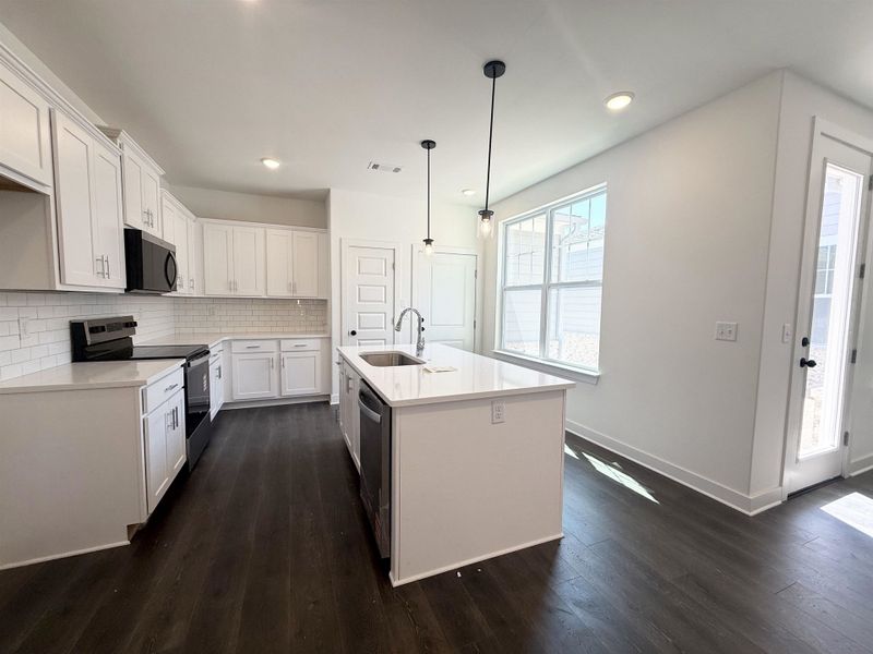 Kitchen featuring stainless steel appliances, a kitchen island with sink, white cabinetry, hanging light fixtures, and backsplash