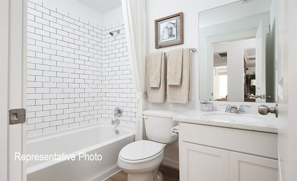 Bathroom featuring a white subway tile shower surround, a built-in tub, white vanity cabinetry with a light-toned countertop, and wood-finish flooring Bathroom featuring a white subway tile shower surround, a built-in tub, white vanity cabinetry with a light-toned countertop, and wood-finish flooring
