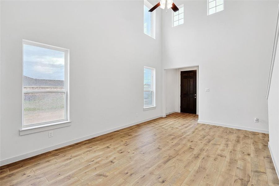 Empty room with ceiling fan, light wood-type flooring, and a towering ceiling