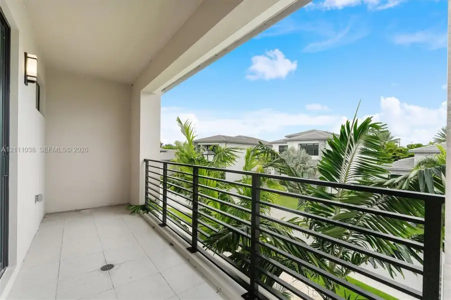 Covered balcony featuring tile flooring, metal railing, and wall-mounted exterior lighting