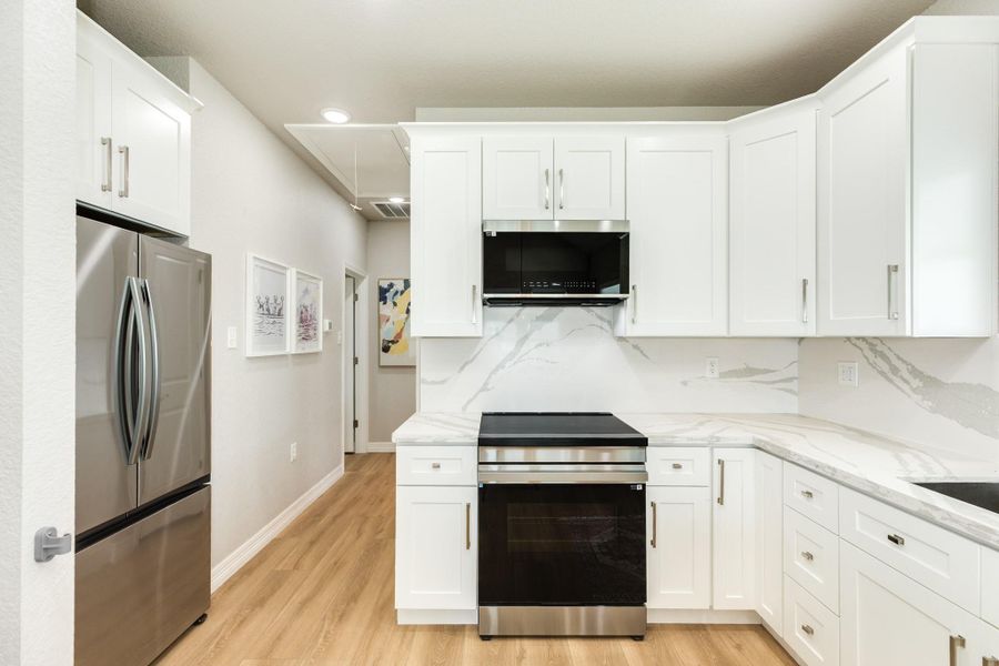 Contemporary kitchen showcases quartz countertops, custom white cabinetry, stainless steel appliances.