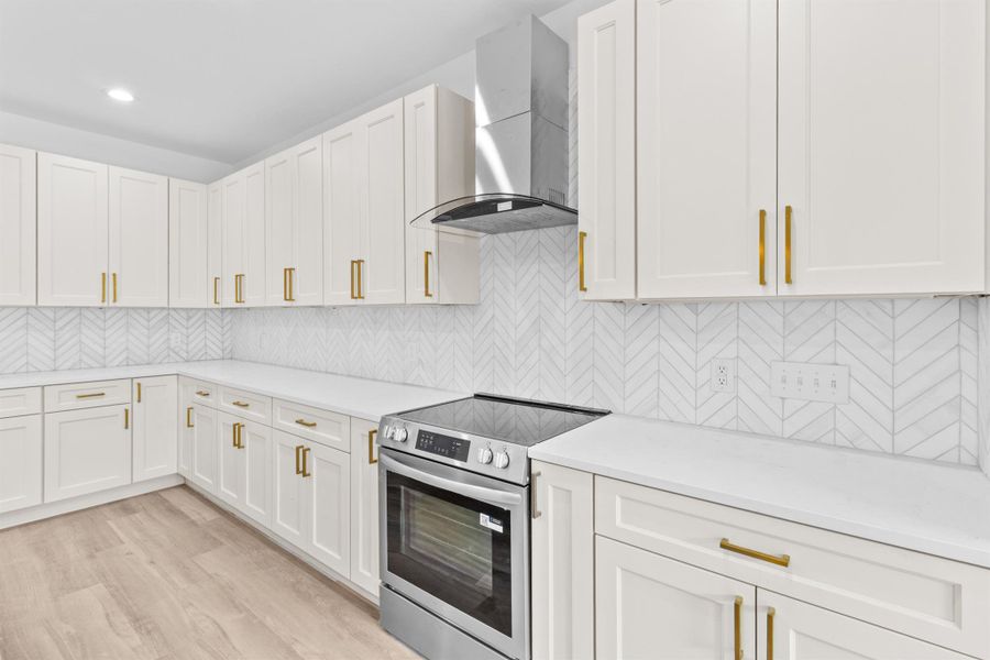 Kitchen featuring stainless steel range with electric stovetop, tasteful backsplash, wall chimney range hood, white cabinetry, and light wood-style flooring