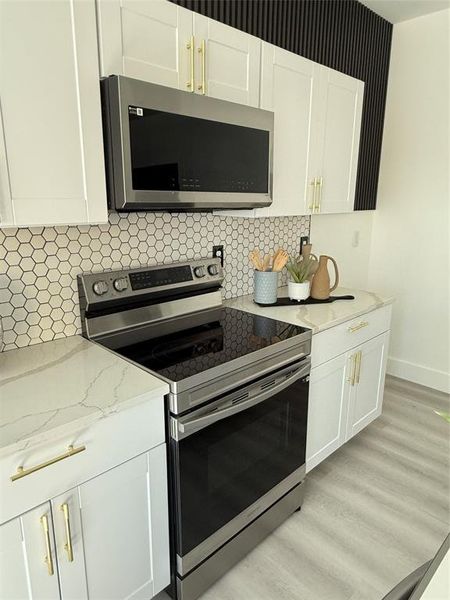 Kitchen with white cabinetry, decorative backsplash, and electric range