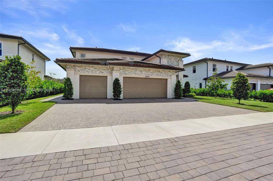 Exterior featuring a multi-car paver driveway, stone facade accents, and mature landscaping