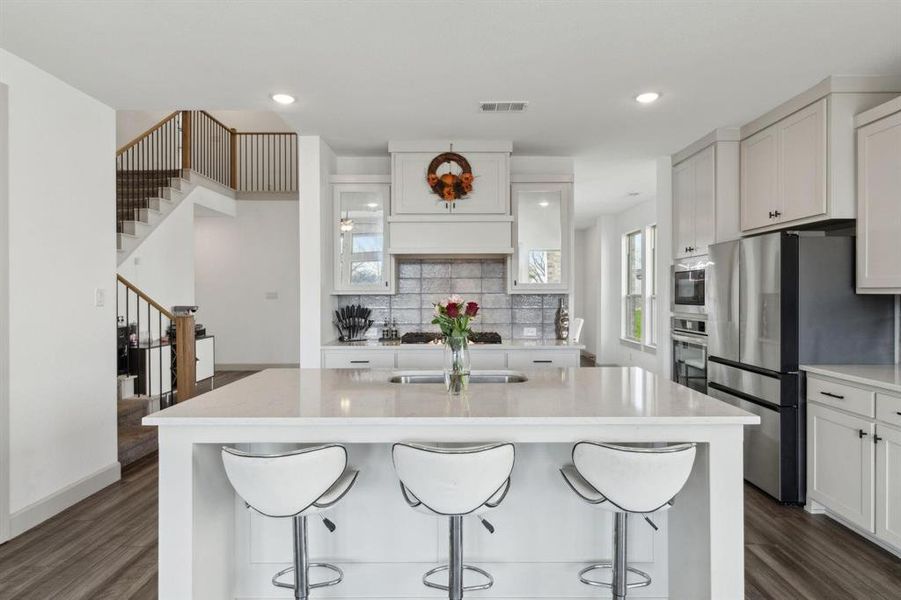 Kitchen featuring white cabinets, stainless steel appliances, an island with sink, light stone countertops, and recessed lighting Kitchen featuring white cabinets, stainless steel appliances, an island with sink, light stone countertops, and recessed lighting
