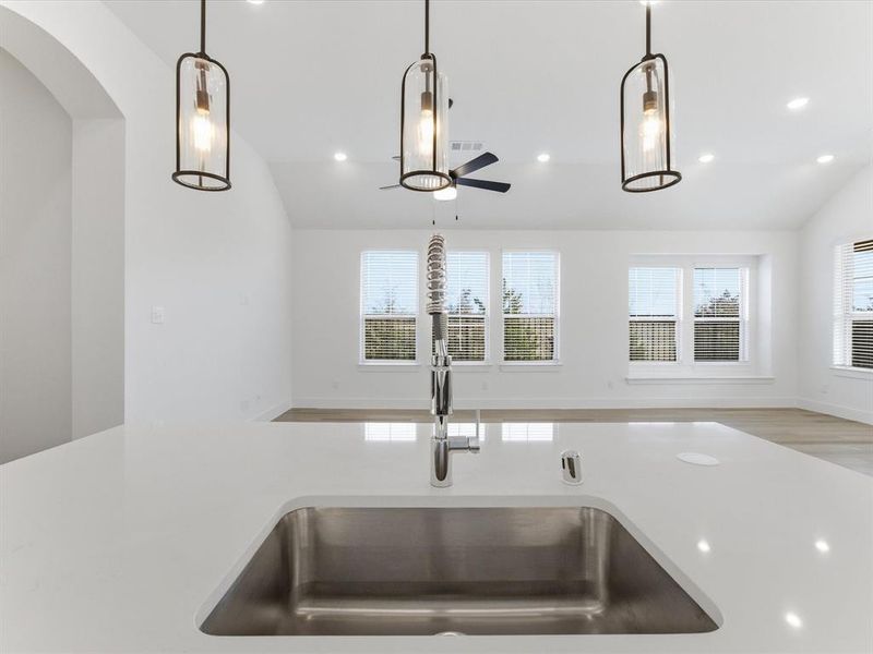 Kitchen view of ceiling fan, decorative light fixtures, and light stone counters