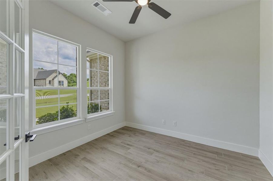 Room featuring French doors with glass panes, wood-finish flooring, and multiple windows with white trim Room featuring French doors with glass panes, wood-finish flooring, and multiple windows with white trim