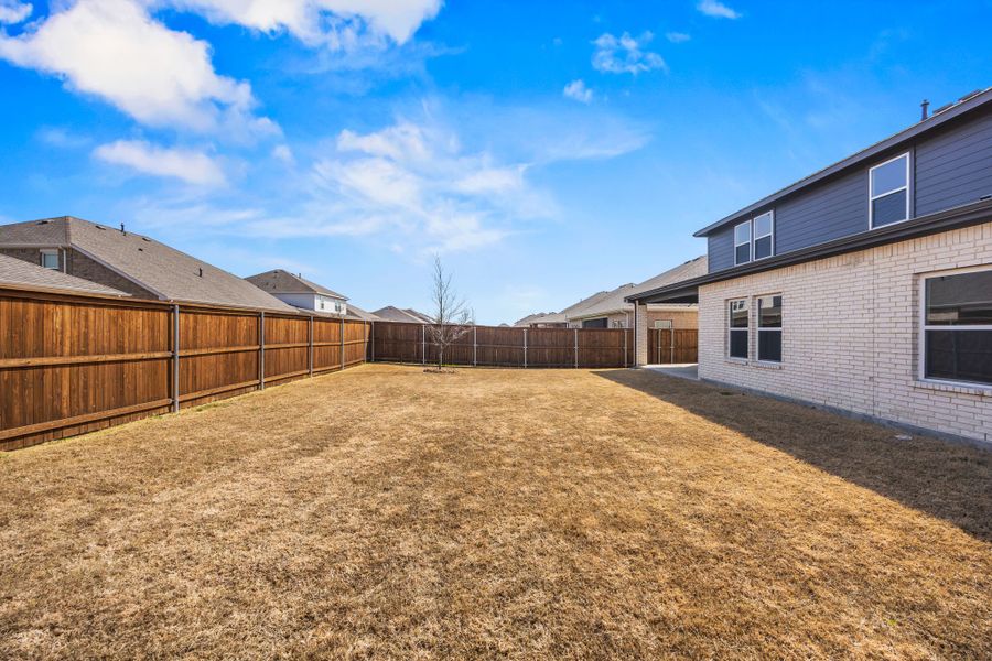 A fenced in yard with a house and a dirt field.