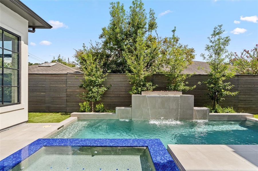 The spa, bordered with vibrant blue tiles, flows seamlessly into the pool while the meticulously landscaped garden and privacy fence provide a tranquil and secluded outdoor environment.