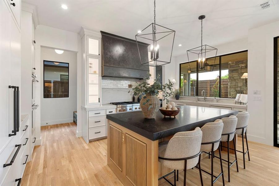 Two tone kitchen featuring a breakfast bar area, a center island, light wood-style floors, two tone color scheme, and dark stone countertops Two tone kitchen featuring a breakfast bar area, a center island, light wood-style floors, two tone color scheme, and dark stone countertops