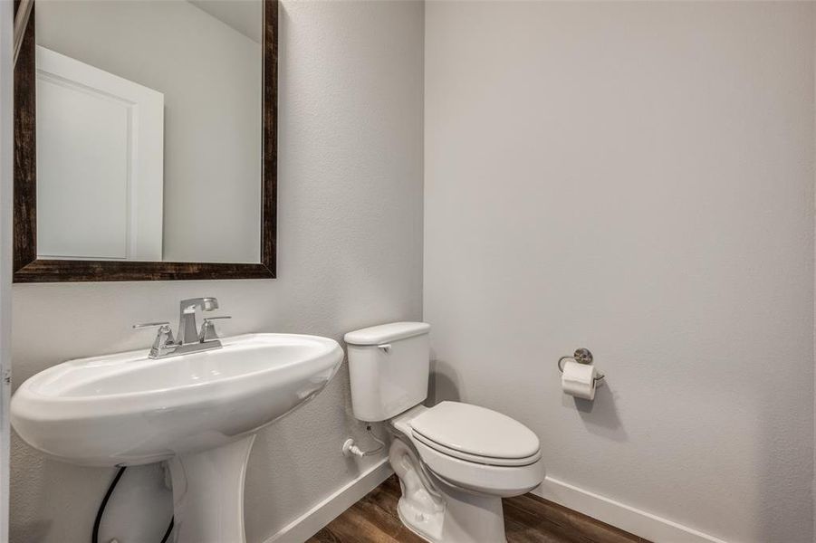 Half bath with toilet, wood finished floors, baseboards, and a sink