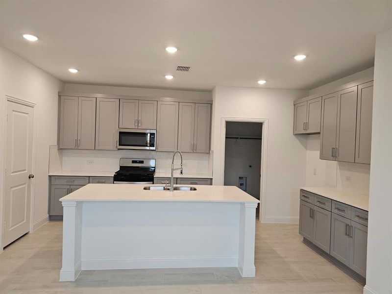 Kitchen with gray cabinetry, tasteful backsplash, stainless steel appliances, light stone counters, and recessed lighting