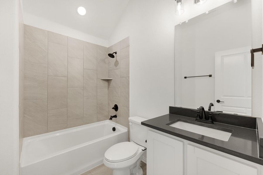 Bathroom with tiled tub-shower combo, white vanity with dark countertop, and black fixtures