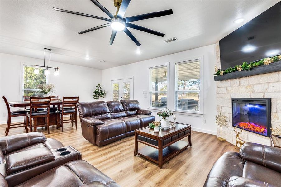 Living area featuring light wood-type flooring, a ceiling fan, a stone fireplace, and plenty of natural light
