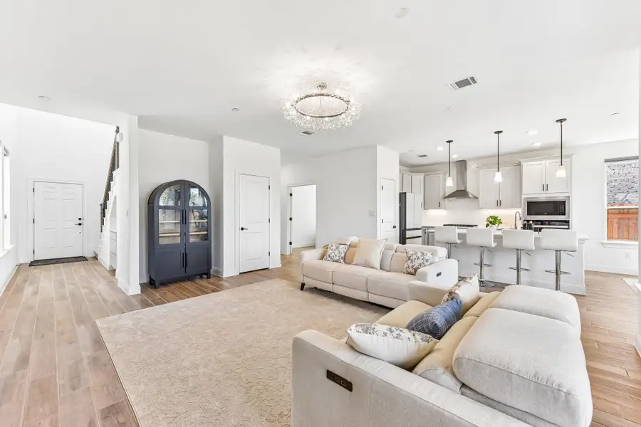 An open floorplan living room with wood flooring extends seamlessly into a modern kitchen.