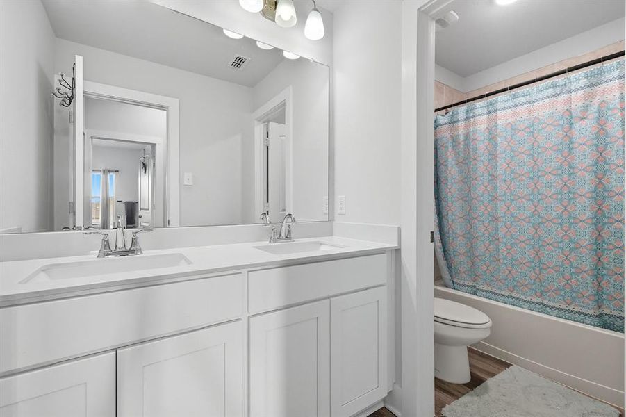Full bathroom featuring shower / bath combo, double vanity, and wood finished floors Full bathroom featuring shower / bath combo, double vanity, and wood finished floors