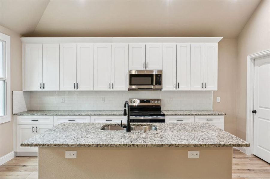 Kitchen featuring light wood-type flooring, light stone countertops, stainless steel appliances, and white cabinetry Kitchen featuring light wood-type flooring, light stone countertops, stainless steel appliances, and white cabinetry