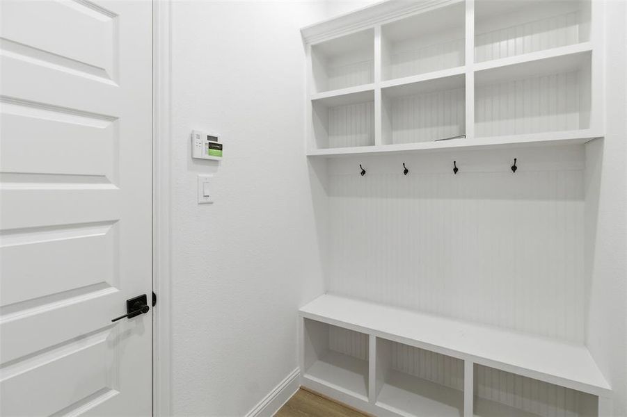 Built-in white storage unit featuring beadboard backing, four upper cubbies, four coat hooks, a bench, and four lower cubbies