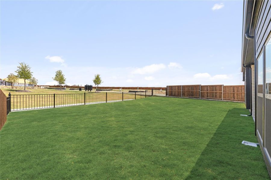 Spacious backyard with green lawn, black iron fence, and wood privacy fence along the perimeter