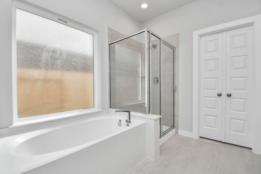 Indulge in a spa-like retreat within the confines of this primary bathroom. Delight in a spacious walk-in shower enveloped in stylish tile surround and unwind in a separate garden tub adorned with custom detailing. Sample photo of completed home with similar floor plan. Actual colors and selections may vary.