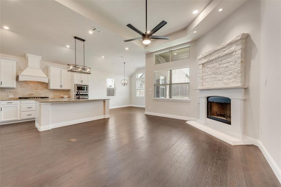 Unfurnished living room featuring a fireplace with raised hearth, dark wood-style floors, ceiling fan, recessed lighting, and a chandelier Unfurnished living room featuring a fireplace with raised hearth, dark wood-style floors, ceiling fan, recessed lighting, and a chandelier