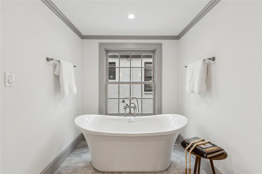 Bathroom featuring a freestanding bath, baseboards, and crown molding