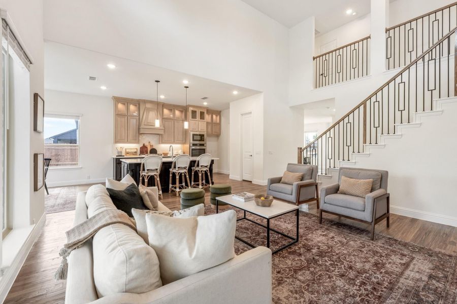 Open-concept living room with high ceilings, staircase, and kitchen visible in background with wood cabinets