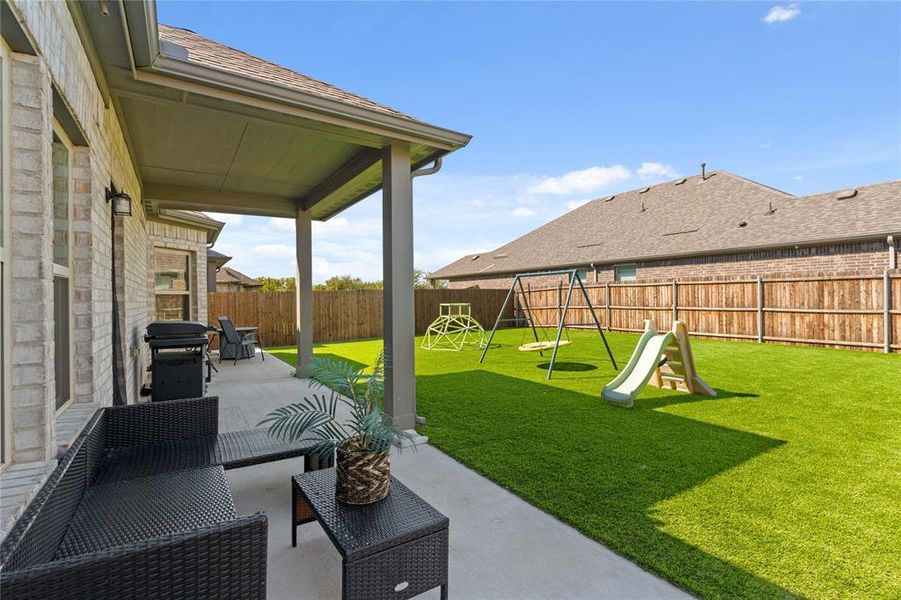 Spacious fenced backyard featuring $25k in patio and turf updates, area for grilling, a playground, and outdoor lounge area